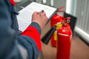 man carrying out a fire risk assessment looking at fire extinguishers with clipboard and pen